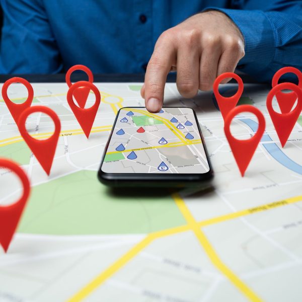 A map with pinned location and a phone with opened Google maps, showing locations. A hand points on maps, and the image illustrates an importance of local SEO.