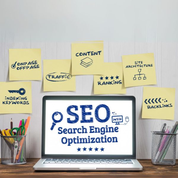 a laptop with SEO - Search Engine Optimization on its screen; yellow notew on a wall behind